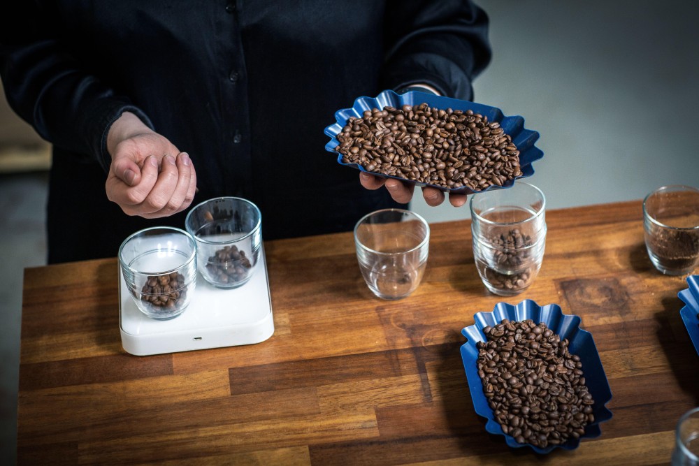 A person weighs coffee beans into glasses on a scale.