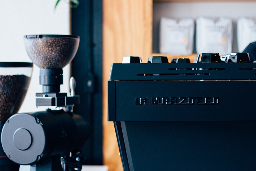 A black La Marzocco espresso machine next to a coffee grinder.