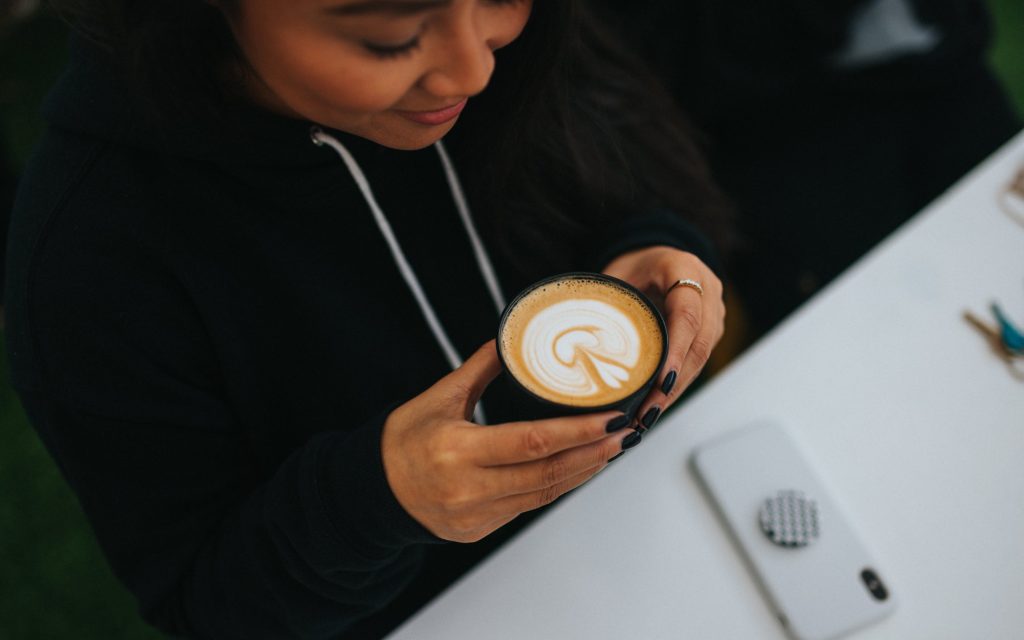 A woman enjoys a cappuccino at a café.