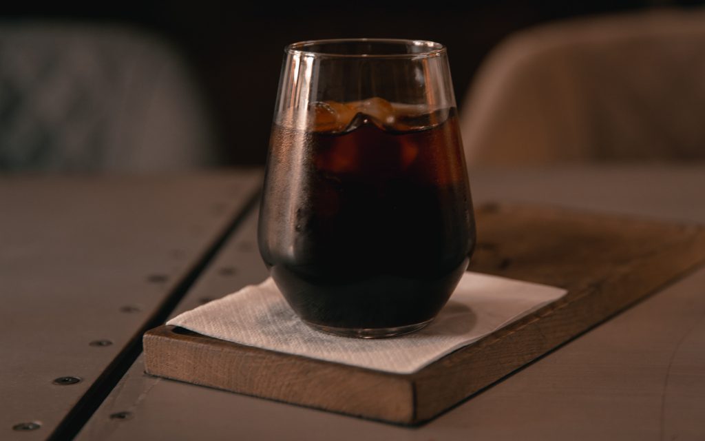 A glass of cold brew on a wooden coaster.