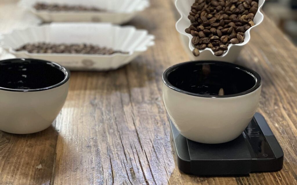 Grãos de café sendo despejados numa tigela sobre mesa de cupping