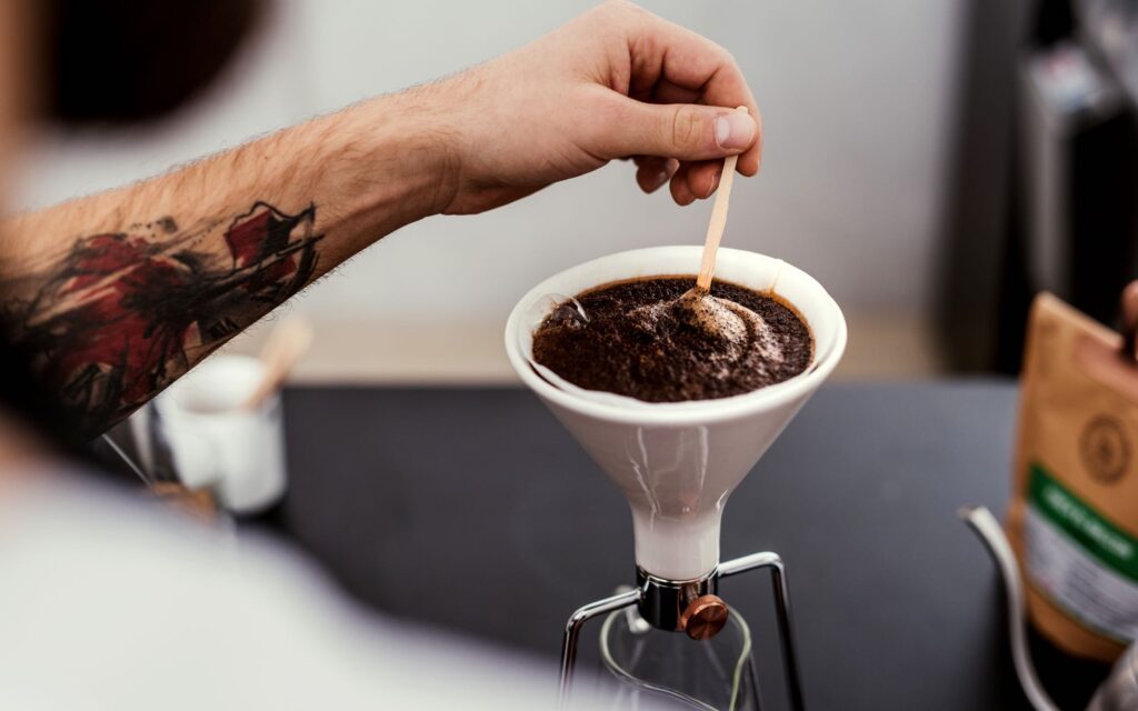 A barista stirs the bloom while using a GOAT STORY GINA brewer.