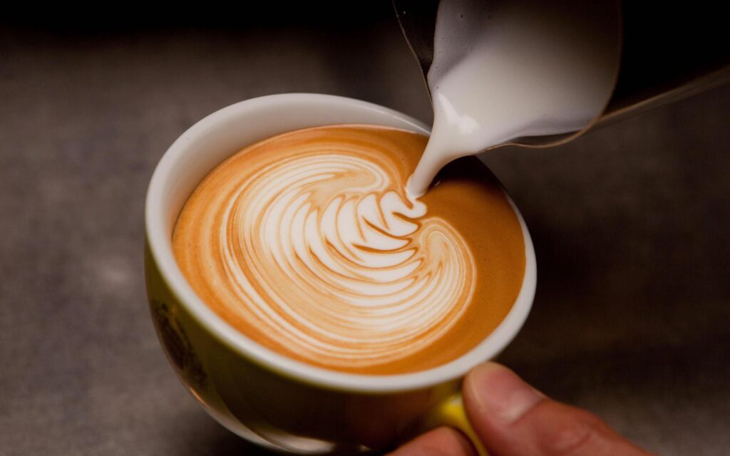 Close de uma xícara de bebida à base de café com leite com latte art sendo preparada