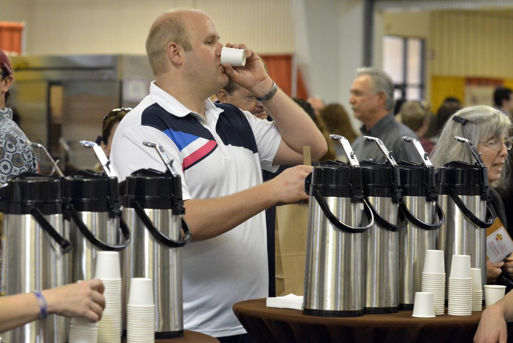 An expo attendee drinks tea samples from a batch brewer.