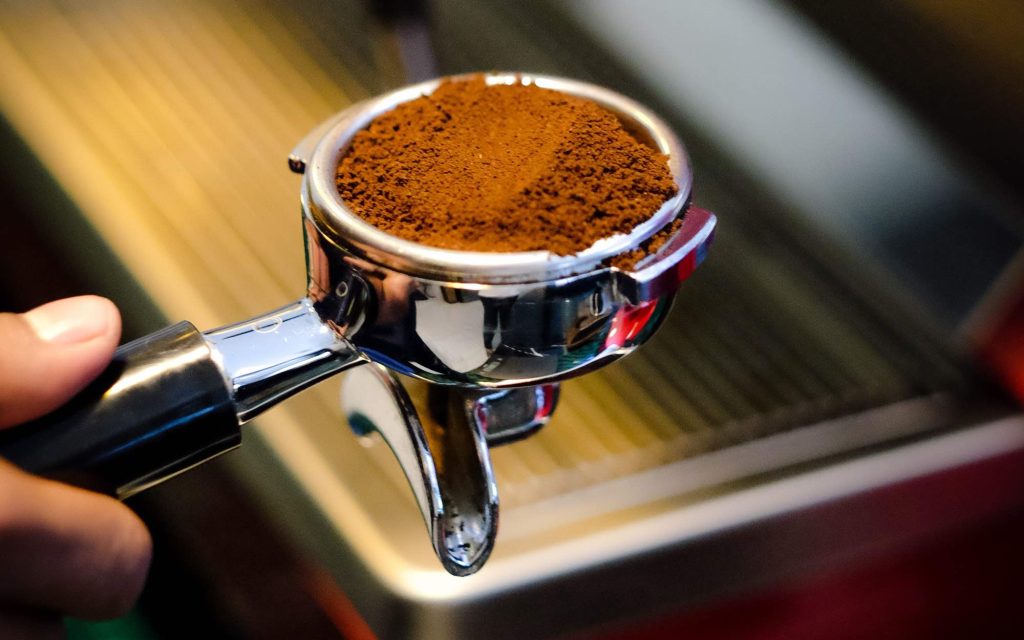 A barista holds a portafilter containing ground coffee.