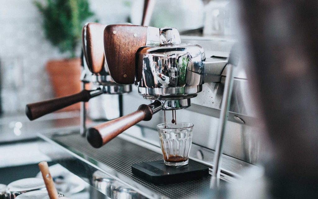 A barista extracts espresso into a glass.