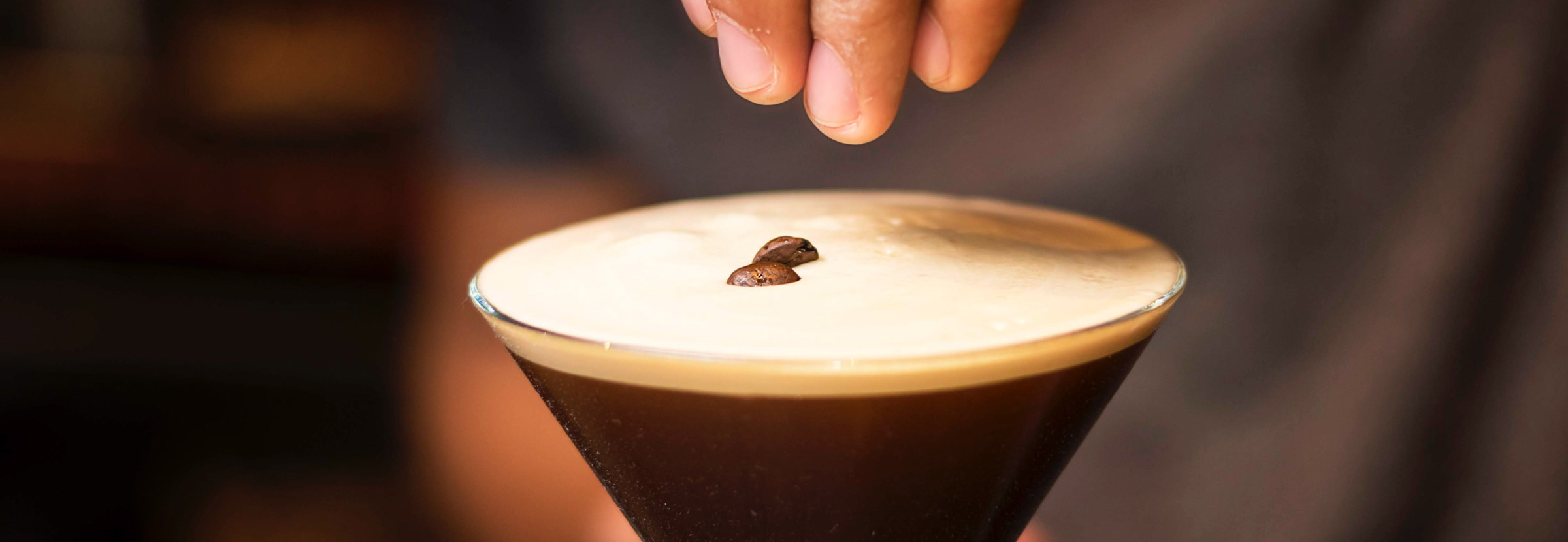 Preparing a coffee cocktail and garnishing it with coffee beans.