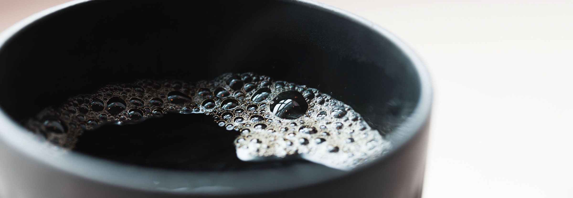 A cup of black filter coffee with bubbles.