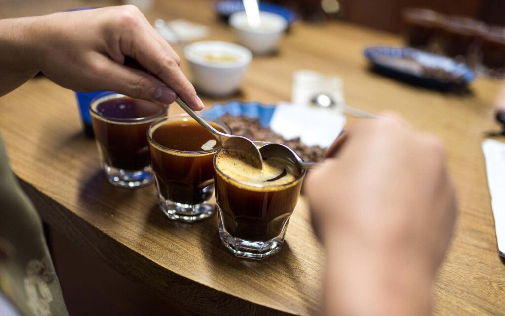 Mãos de um provador removendo a crosta de uma amostra de café durante uma sessão de cupping