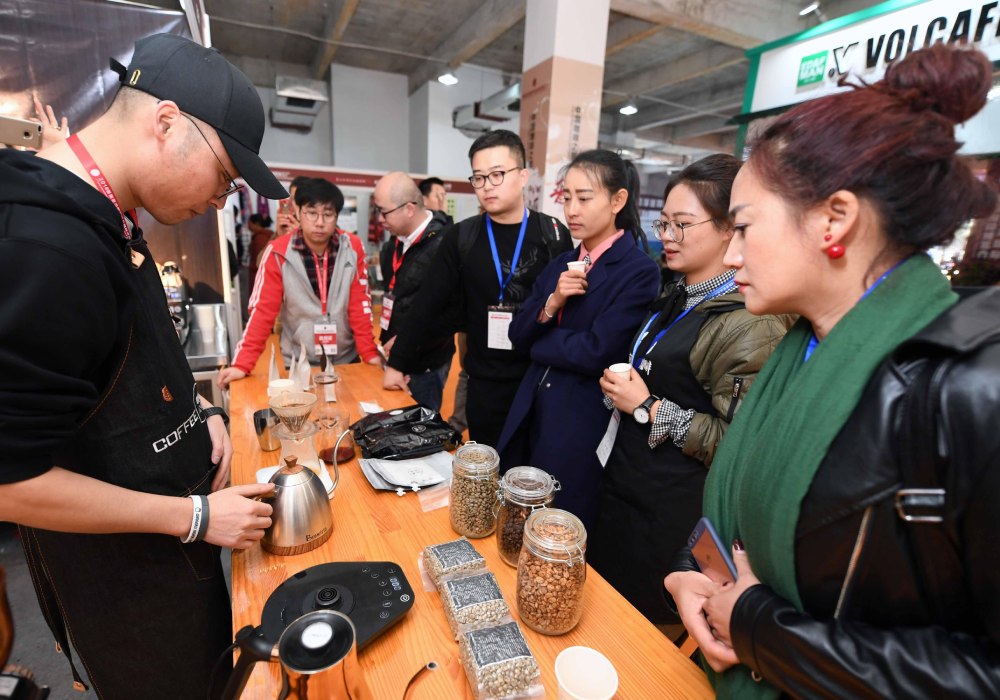 Trade show attendees watch coffee being brewed at a stand.