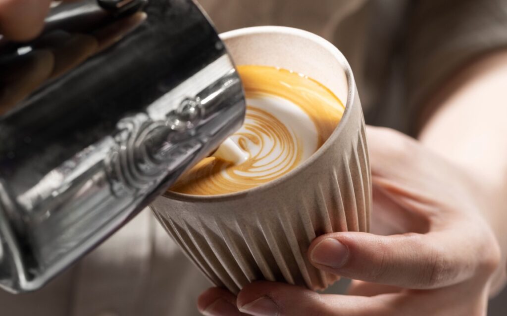 A barista pours latte art in a white HuskeeCup, which is made from recycled coffee husk waste.