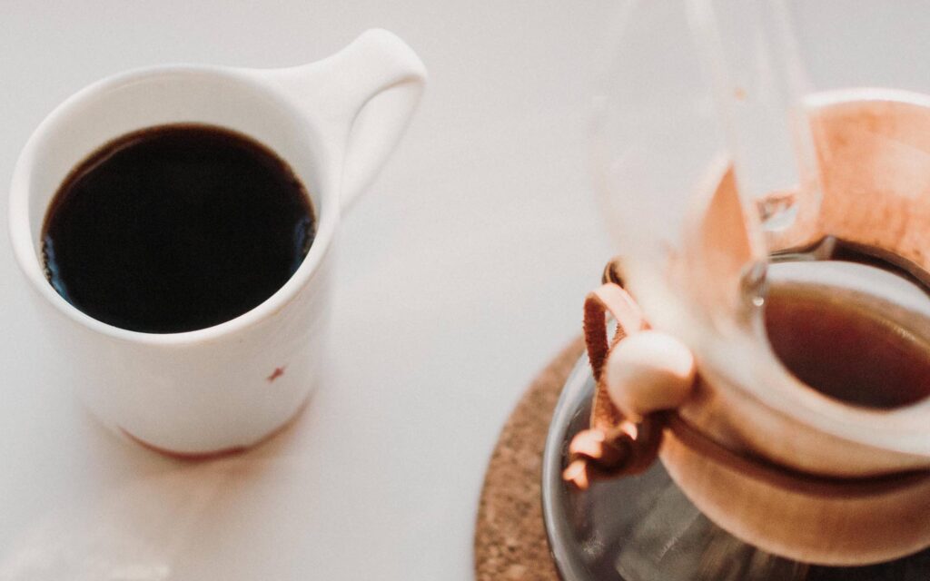 A mug of filter coffee next to a Chemex.