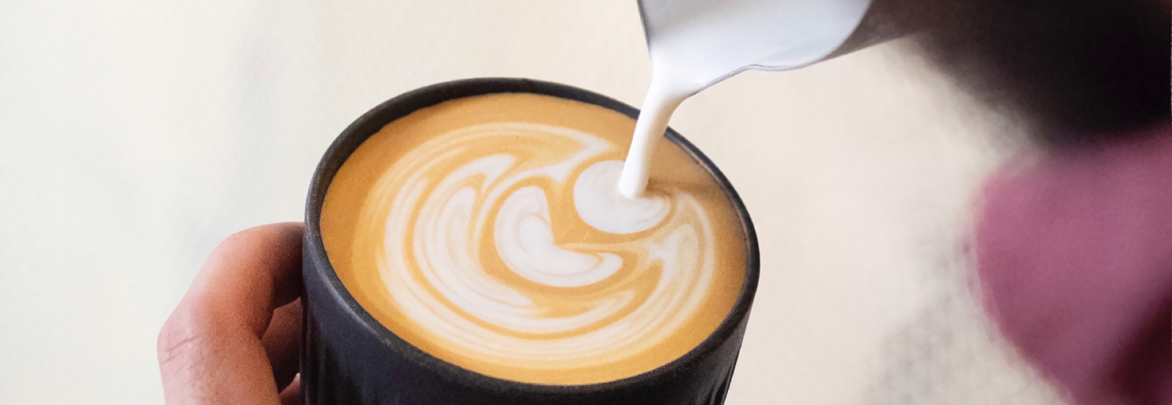 A barista pouring latte art in a black HuskeeCup.