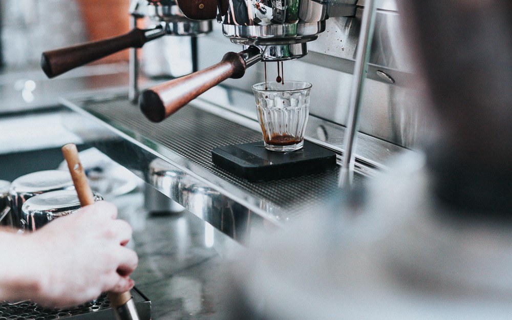 A barista extracts a double shot of espresso into a glass in a coffee shop.